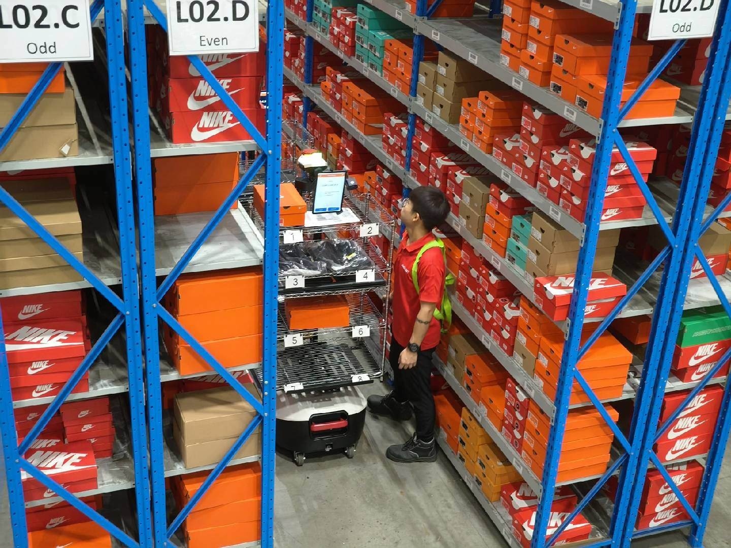 Picker working an order-to-person AMR station in a live shoe-storage warehouse
