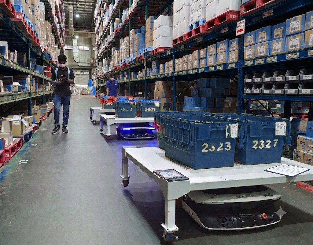Syrius AMRs carrying tote-laden carriers down a live warehouse aisle